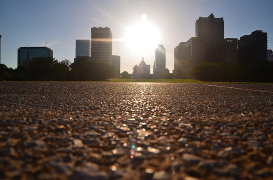 Surface Level View Of Street With Cityscape In Background At Sunset