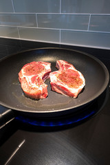 Closeup of Two Pork Chops Frying in a Non-Stick Frying Pan on an Induction Stove Top