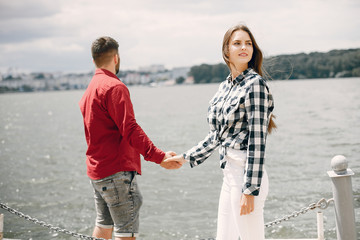 Cute couple in a park near river. Lady in a chirt. Guy in a red shirt