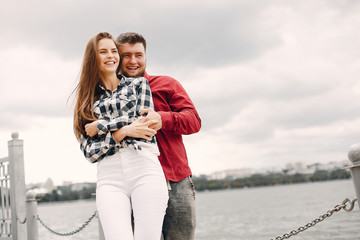 Cute couple in a park near river. Lady in a chirt. Guy in a red shirt