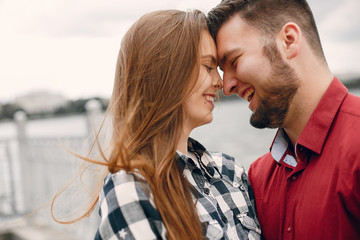 Cute couple in a park near river. Lady in a chirt. Guy in a red shirt