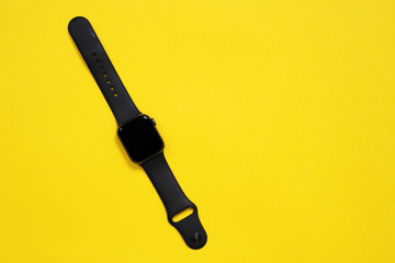 May 01, 2020, Rostov, Russia: Smart gadget Apple Watch S4 of space gray color for monitoring notifications and activity, aluminum case with black sport band on yellow background, top view, copy space.