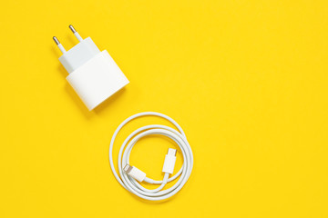 Wrapped in a ring USB lightning cable and power adapter for charging smartphones and devices or for connecting gadgets to a computer or laptop on yellow background, top view, copy space. - obrazy, fototapety, plakaty