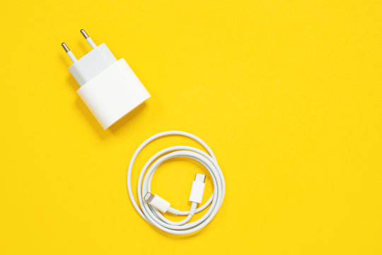 Wrapped in a ring USB lightning cable and power adapter for charging smartphones and devices or for connecting gadgets to a computer or laptop on yellow background, top view, copy space.