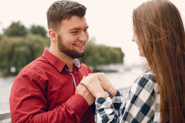 Cute couple in a park near river. Lady in a chirt. Guy in a red shirt