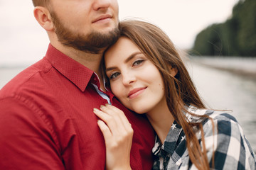 Cute couple in a park near river. Lady in a chirt. Guy in a red shirt