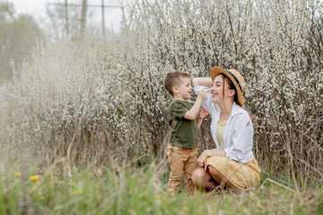 Happy mother and son having fun together. Mother gently hugs her son. In the background white flowers bloom. Mother's day