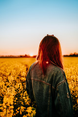 girl in a denim jacket stands on a canola field at sunset