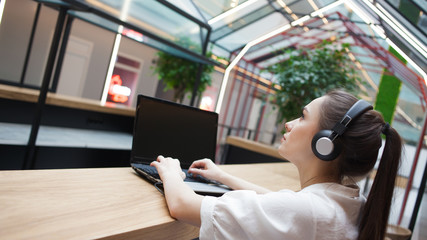 Lifestyle portrait in the interior. A young woman with headphones works at a laptop