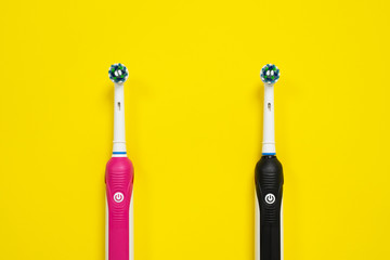 Black and pink electric toothbrushes with replacement heads, for boy and girl on yellow background, top view, copy space. Modern devices for daily health care, oral hygiene.