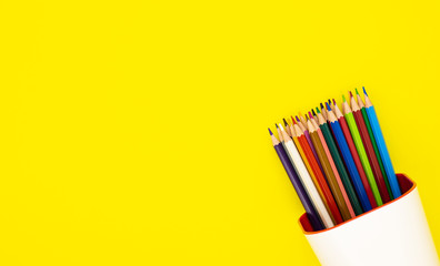 colored pencils in a white organizer, isolated on a yellow background. office supplies for preparing for school. background for designers with space for text