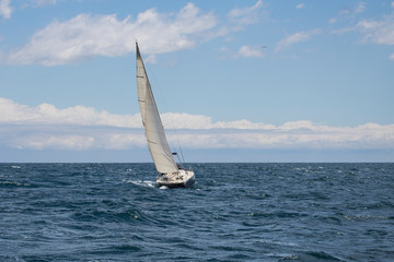 Fototapeta na wymiar A sailing boat navigating in front of Barcelona coast line during a stormy winter afternoon.
