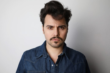 Close-up portrait of bearded man in the denim outfit with bright white t-shirt posing over white wall. Isolated.