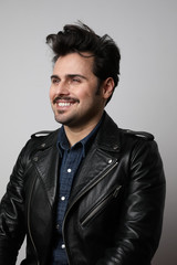 Vertical shot of happy young hipster man in a leather jacket and denim shirt posing over a white background.