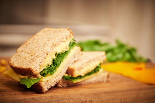 Saludable y liviano sandwich de rucula, queso y pasta de garbanzos, cortado a la mitad, sobre una tabla de madera con hojas de rucula desenfocadas en el fondo
