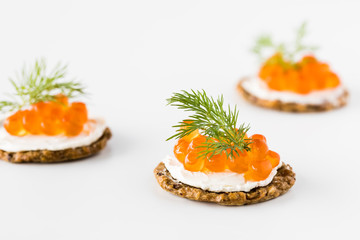 A close up view of cracker and cream cheese canapes topped with red caviar and garnished with dill.