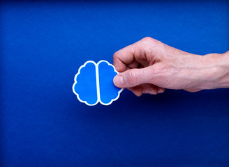 Illustration cerveau tenue par main homme sur fond studio bleu : imaginer, création, créatif,...