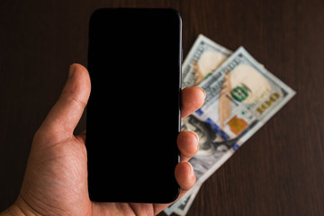 black cellphone  and some bills  on a wooden desk
