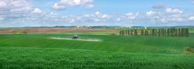 Panoramic view of the hills of green fields in the spring, sprayer fertilizes with fertilizers,...