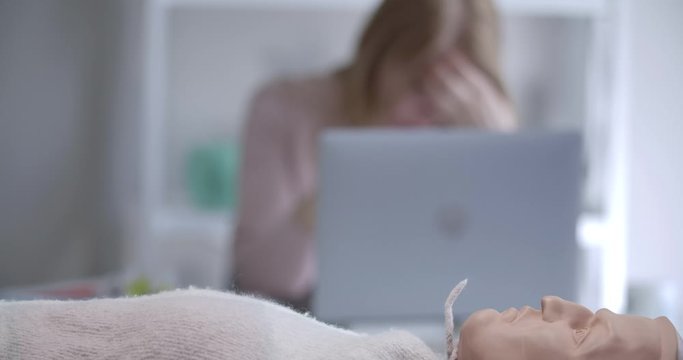 Male hands doing external heart massage on mannequin as blurred woman talking at laptop at the background. Medical workers practicing first aid. Health care, medicine. Cinema 4k ProRes HQ.