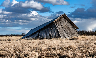 Collapsed traditional scandinavian unpainted wooden shed in field, farmers kept machines and tools...