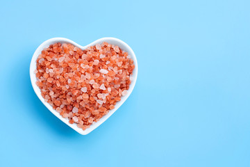 Fototapeta na wymiar Pink himalayan salt in heart shape bowl on blue background.