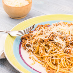 Plate with a portion of spaghetti bolognese and grated cheese close-up - traditional Italian cuisine