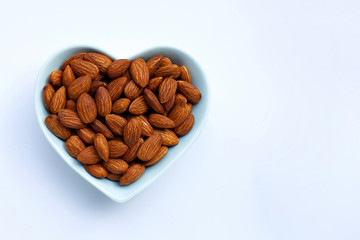 Almonds in heart shape bowl on white background.