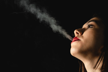 Low key close-up young woman smoking cigarette on black background. Copy space for text message.