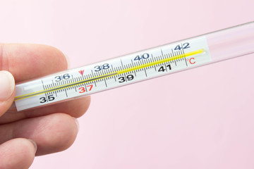 Mercury thermometer in hand on pink background. Close up photo. Thermometer shows a temperature of 38.7 degrees Celsius