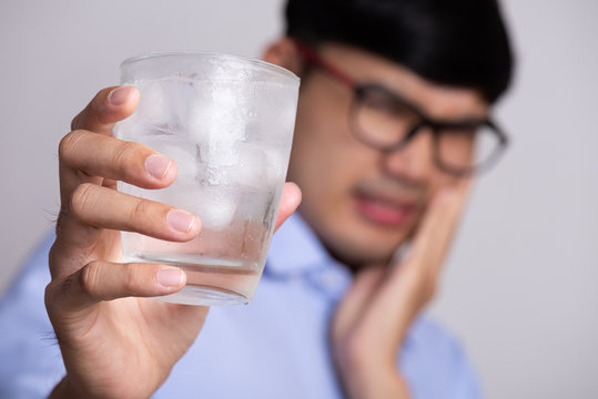 Young man with sensitive teeth and hand holding glass of cold water with ice. Healthcare concept.
