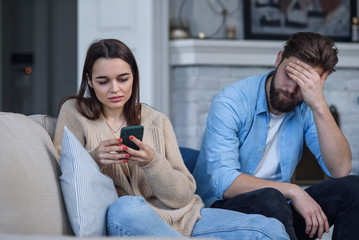 Modern couple at home. Man and woman concentrated on messaging with smartphones, ignoring each...