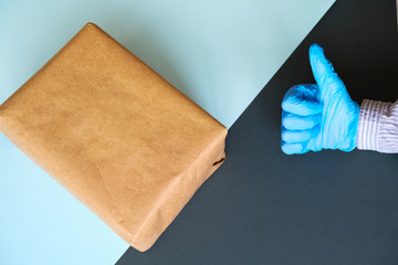Contactless delivery concept. Parcel and courier's hand in protective glove showing thumbs up.
