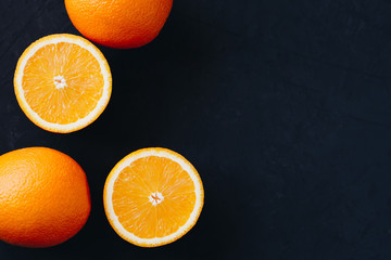 Halves and slices of fresh juicy oranges on black textured background.