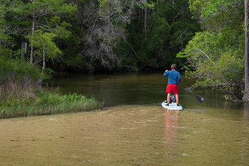 Man using paddle board down shallow creek