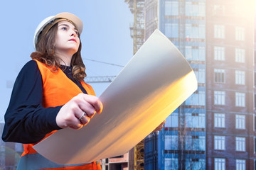 Woman works as a builder. Girl in the form of a builder holds a sheet of paper. Concept - architect oversees the construction. Career in a construction company. Woman next building under construction