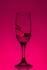 Water pouring into glass. water splash in glass on glowing background. transparent liquid splashing in wine glass.