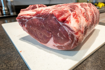 A large cut of raw prime rib beef. The male cuts the thick meat with a large stainless steel knife. The meat is on a white cutting board. The beef has ribs and marbling.