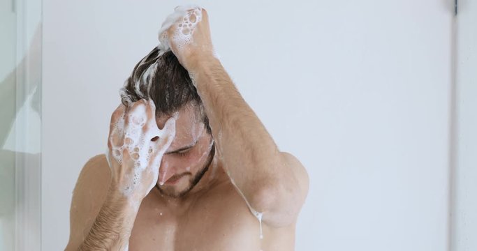 Young handsome bare man washing head with anti-dandruff shampoo lathering hair with foam. Attractive naked guy taking shower doing everyday fresh clean male haircare hygiene routine concept.