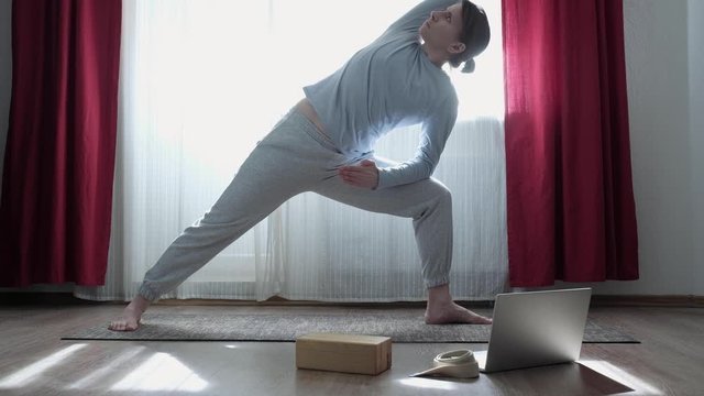 Woman doing Triangle yoga pose, Trikonasana, stretching exercise at home