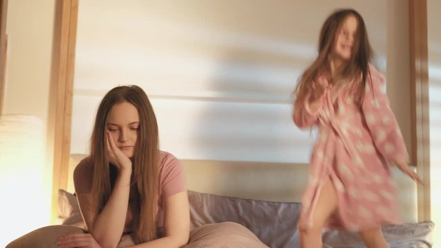 Kid discipline. Trouble parenting. Depressed mother sitting tired with energetic daughter dancing on bed.