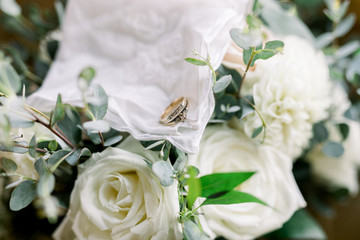 A Set of Antique Gold Wedding Rings on a White Handkerchief Sitting on a Bouquet of White Roses with Carnations and Green Leaves 