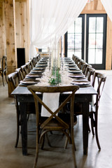 Beautiful Table at a Wedding Reception Set with Gray Plates, Decorated with White Cheesecloth Runner, Green Leaves and Candles in a Glass Vase