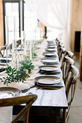 Long Dining Table at Wedding Reception Decorated with a Row of Gray Plates with Gold Forks. The Center of the Table is accented with olive leaves, candles, and a loose runner made of cheesecloth. 