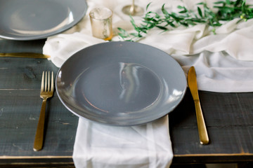 Beautiful Gray Plate with Gold Fork and Knife with Gold Votive Candles, Cheesecloth Runner, Ivory Napkin, Green Garland at a Wedding Reception, Table Design. 