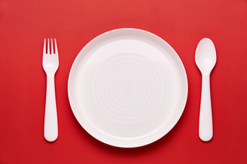 Plasic white cutlery set with red background. Top view