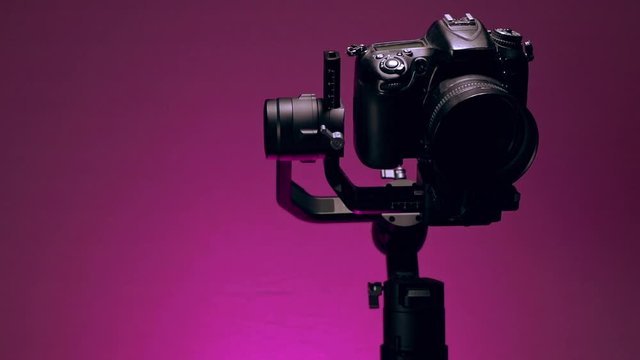 Estabilizador o Gimbal con una camara montada, haciendo movimientos de grabacion con fondo de color violeta