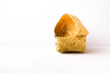 Small empty hand-woven bamboo wicker container placed side way in its lid over white. Focus on...