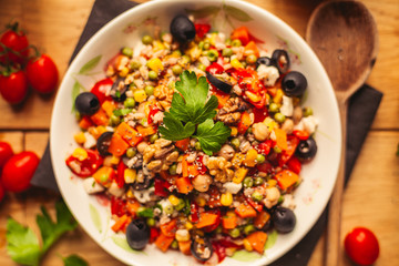 A view of a spelled dish on wooden background with some ingredients around: carrots, peppers, tomatos, parsley and oil