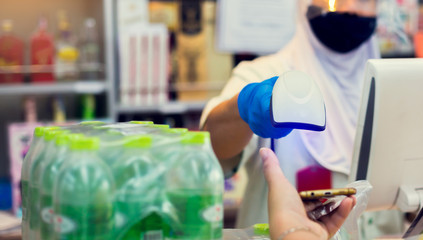 Selective focus to barcode reader in hand of cashier in supermarket. Blurry cashier wearing face shield and mask to protect Coronavirus from many customer.